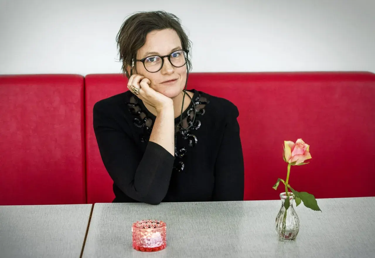 Agnes Lidbeck med familj, en kvinna med glasögon och en blomma på bordet, sitter vid ett rött bås.