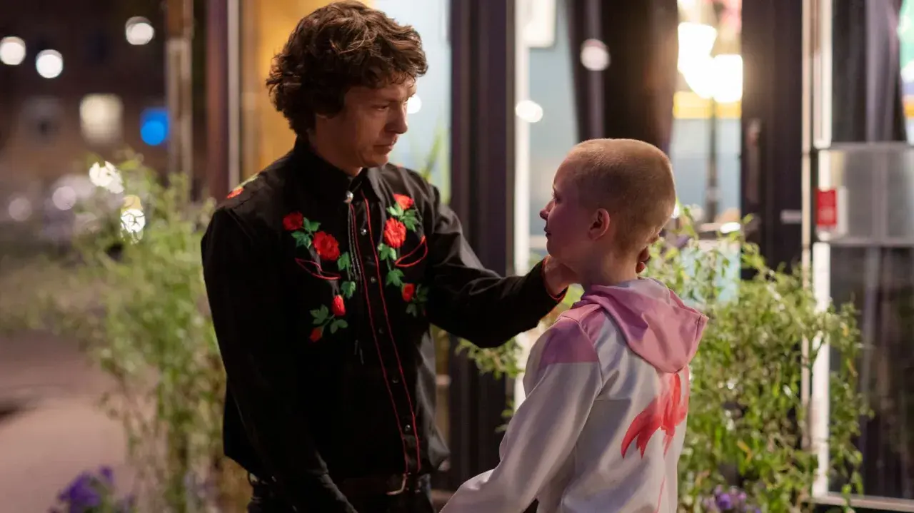 En man med blommig skjorta rör vid ett barns kind. En scen som kan ingå i svenska komedier.