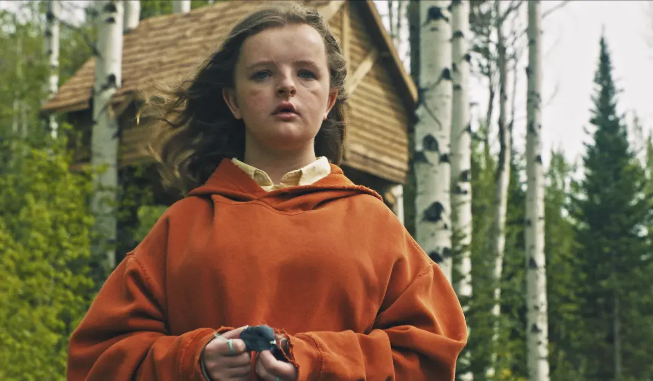 Charlie i orange hoodie, med en fågel i händerna, framför ett trädkoja i skogen. En scen från rollistan i Hereditary.