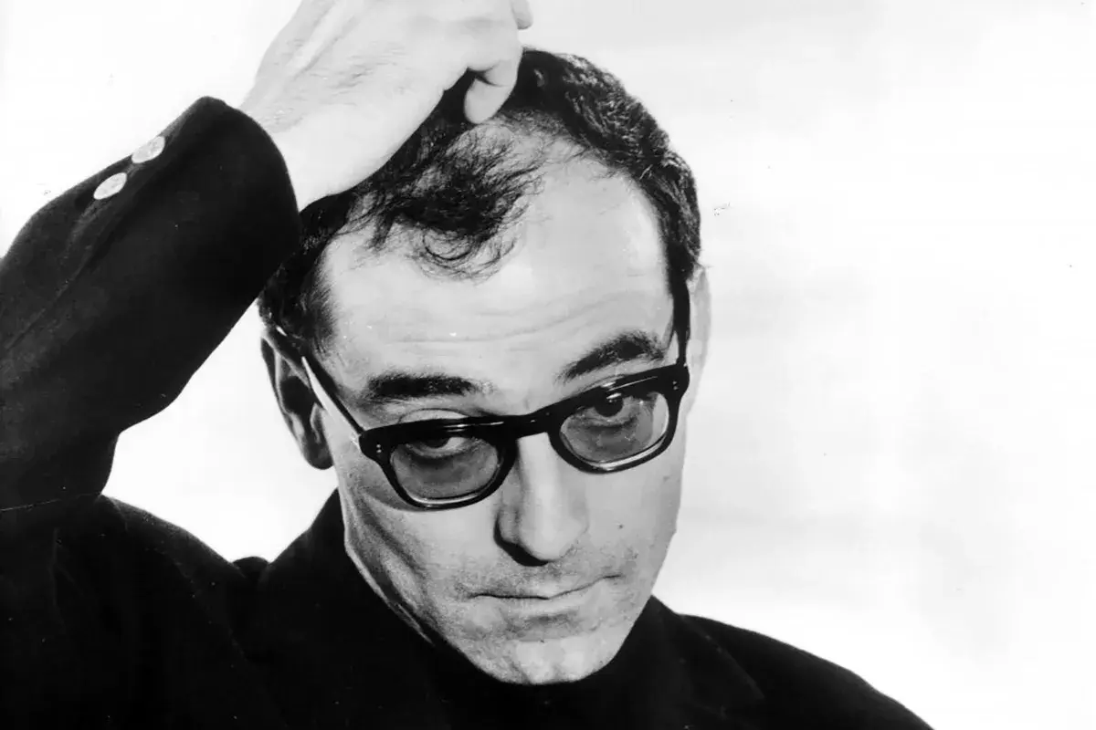 Jean-Luc Godard med handen i håret, bär glasögon och en mörk kavaj. En ikonisk bild av filmskaparen.