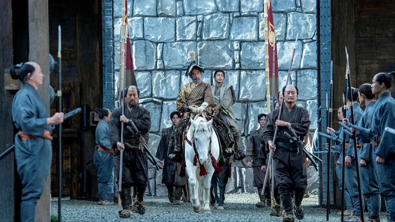 En ståtlig shogun på vit häst, omgiven av sina samurajer, anländer till en befästning. Scen från shogun serie.
