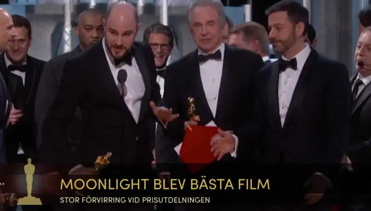Män i kostym på scenen, en håller en Oscarstatyett och en röd mapp. Texten "MOONLIGHT BLEV BÄSTA FILM" syns.