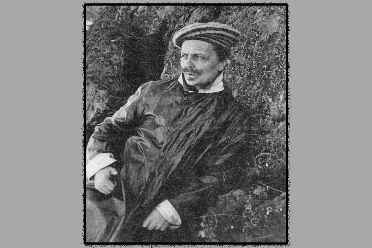 August Strindberg, klädd i rock och randig mössa, vilar mot en stenig bakgrund. Han ser ut som om han funderar på sitt nästa verk.