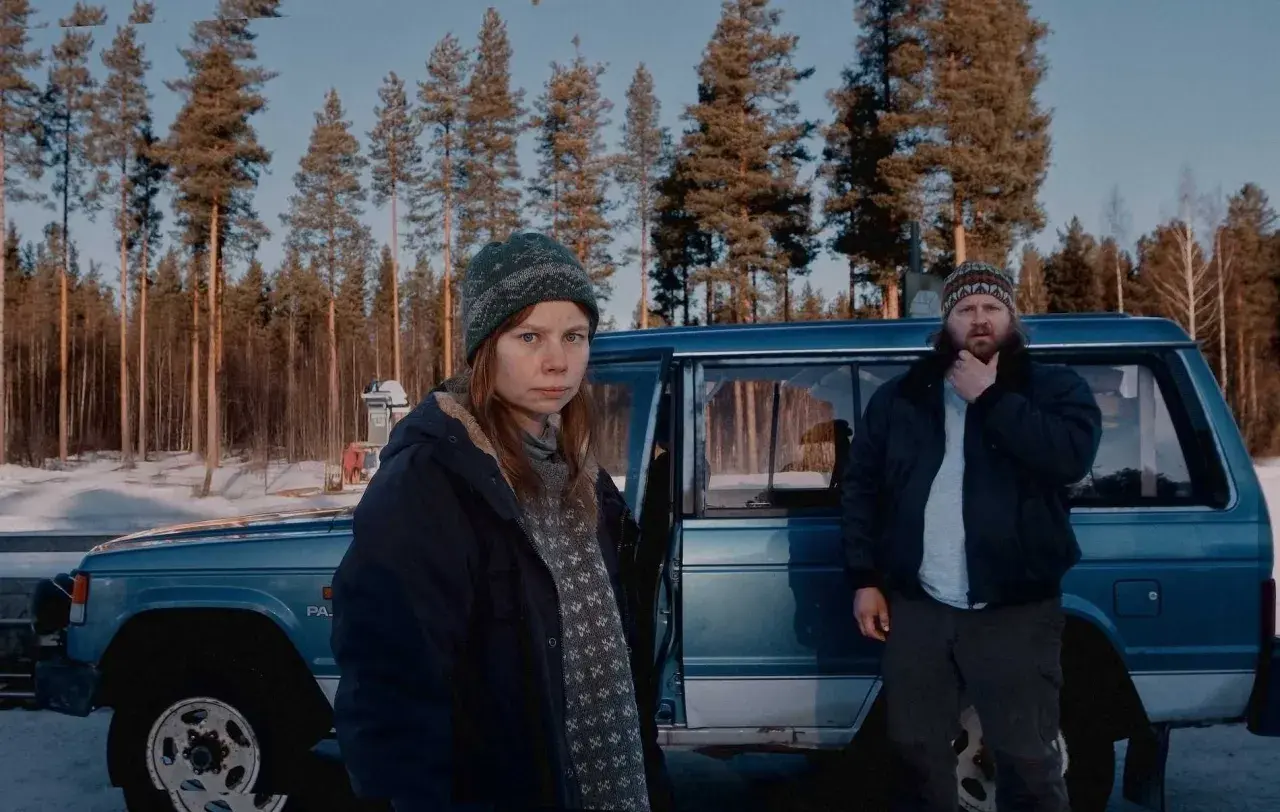 Två personer står vid en blå bil i en snöig skog. Kanske jag for ner till bror serie, och detta är en scen från den.