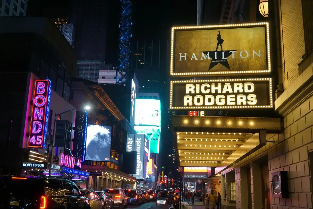 Broadway-skyltar lyser upp natten. Hamilton musikal visas på Richard Rodgers Theatre, omgivet av neonljus och trafik.