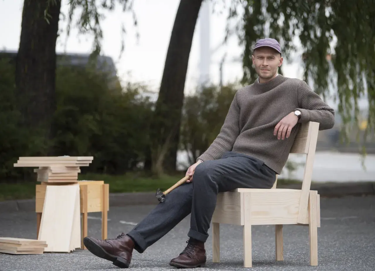 Erik Eje Almqvist sitter på en trästol med en hammare i handen, omgiven av trämaterial.