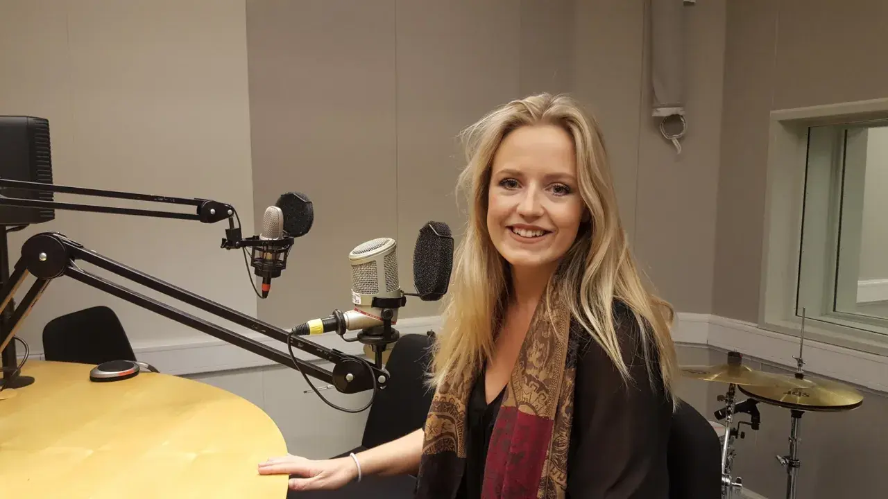 Maria Broberg ler i en radiostudio med mikrofoner och trummor i bakgrunden.