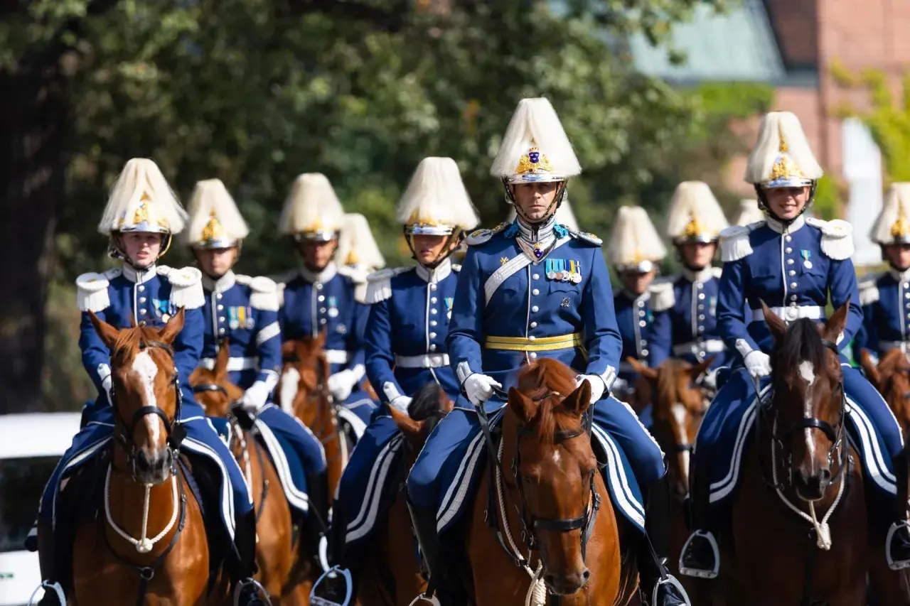 Livgardet i sina blå uniformer och höga hattar rider på bruna hästar.