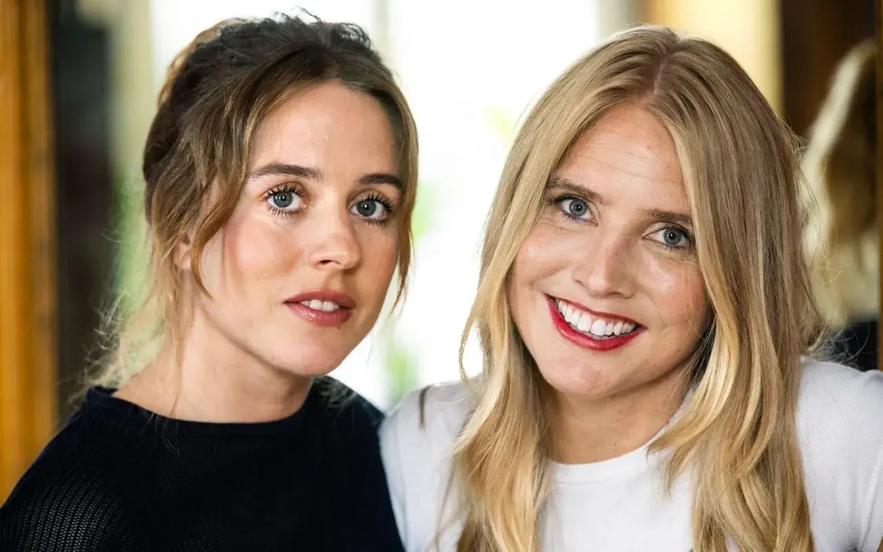Två kvinnor, en med brunt hår uppsatt, den andra med blont hår, ler mot kameran. Amanda Romare är en av dem.