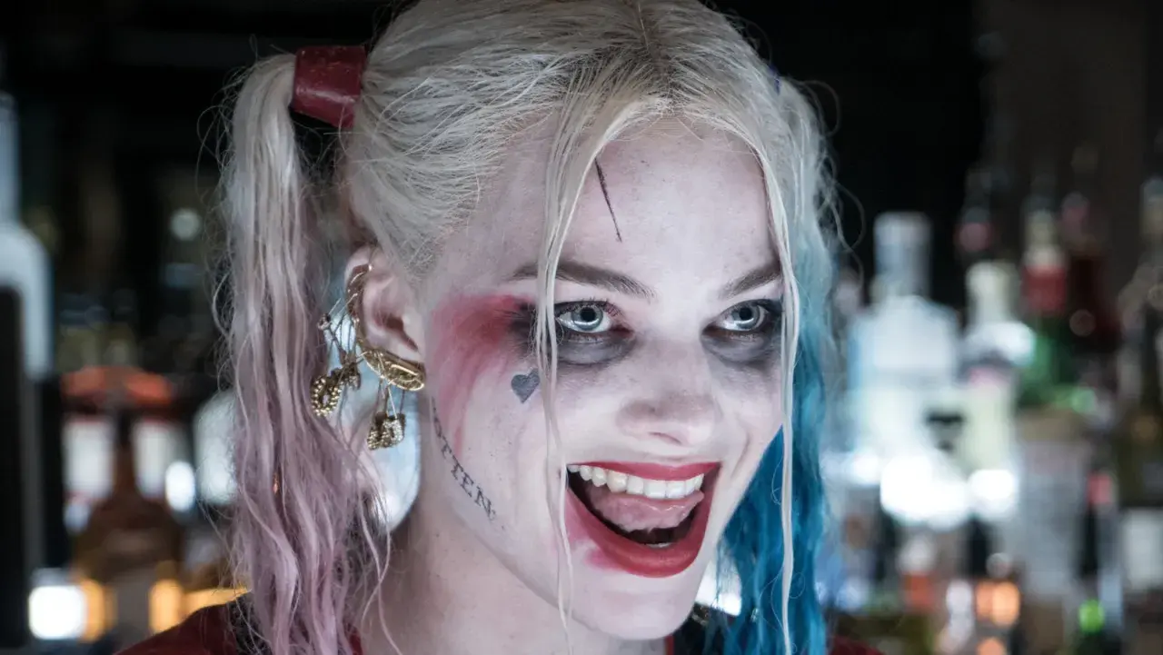 Margot Robbie som Harley Quinn, med sitt karaktäristiska smink och frisyr, ler galet.
