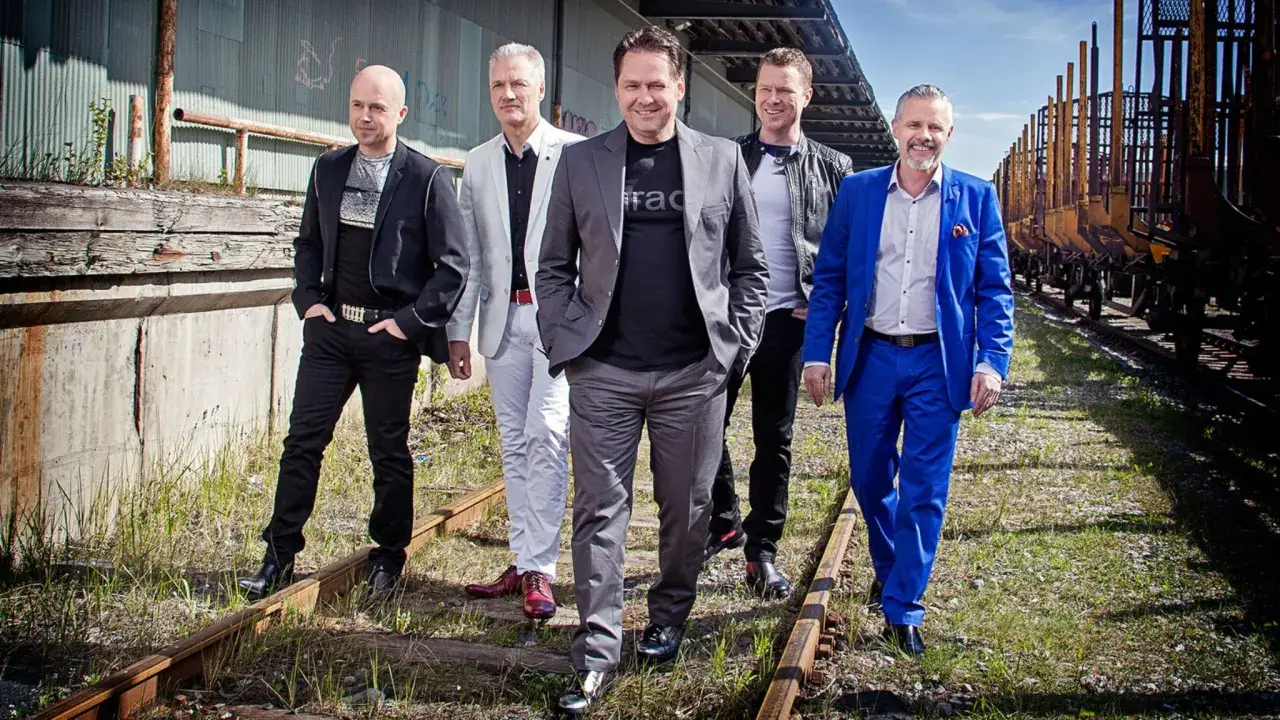 Fem män i kostym står på ett järnvägsspår. De ser ut som om de är redo för en spelning med black jack dansband 1990.