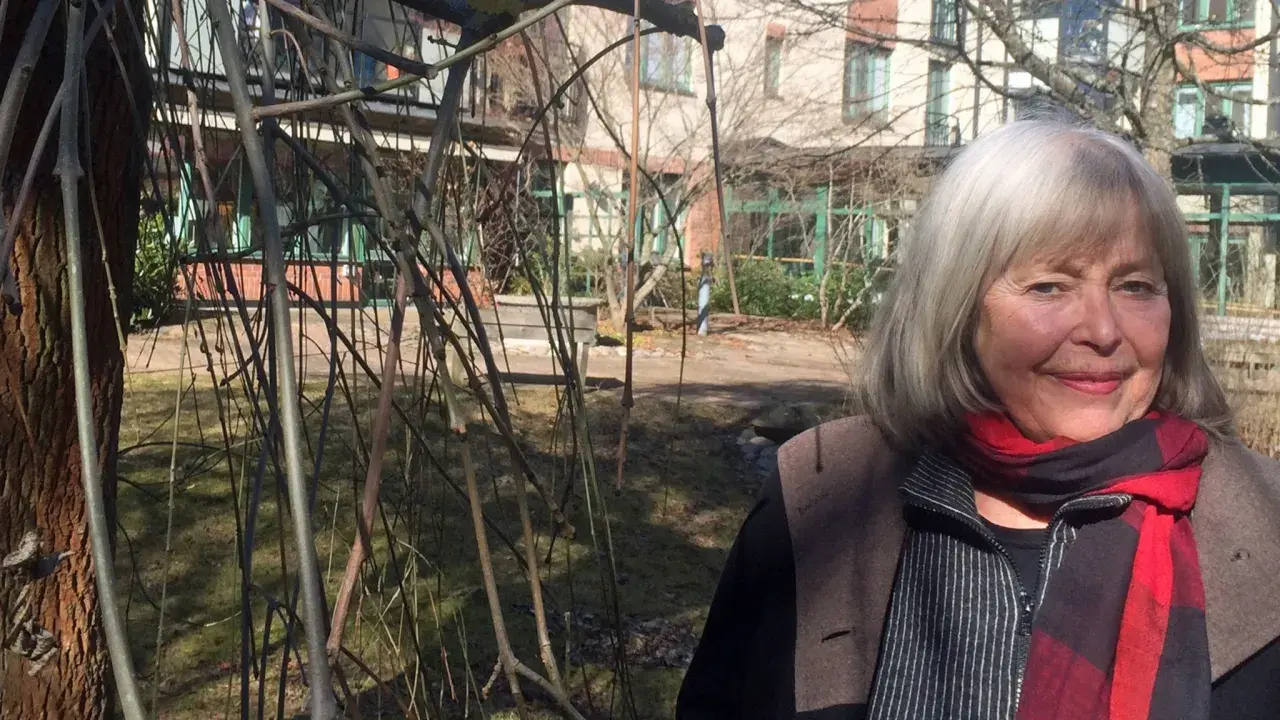 Agneta Pleijel ung, med grått hår och röd halsduk, ler mot kameran i en trädgård.