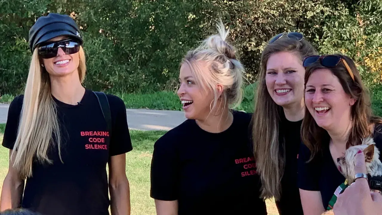 Paris Hilton och vänner ler glatt utomhus, alla bär svarta t-shirts med texten "Breaking Code Silence", som om de är med i en serie om sekt.