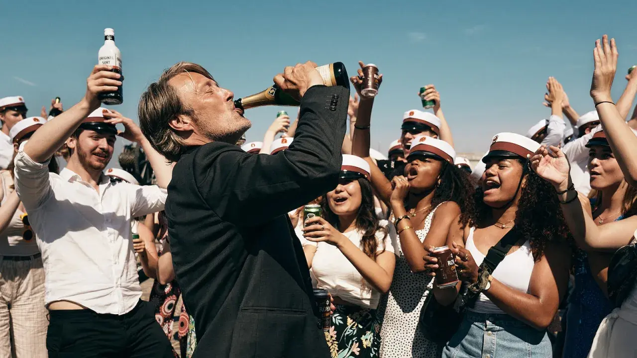 Mads Mikkelsen dricker ur en champagneflaska, omgiven av glada studenter med studentmössor. En runda till recension av firandet.