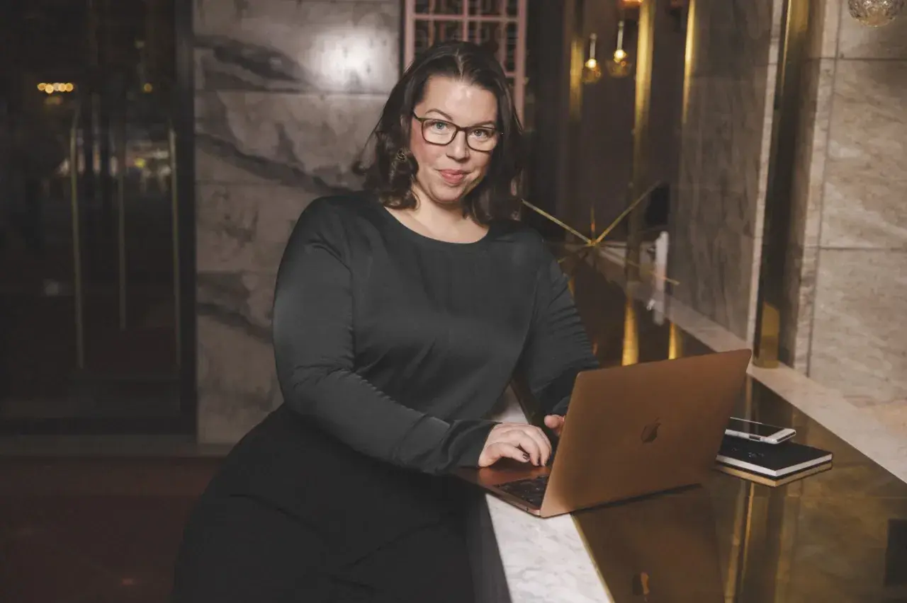 Linnea Molander, med glasögon och svart klänning, arbetar vid en bärbar dator i en lyxig miljö.