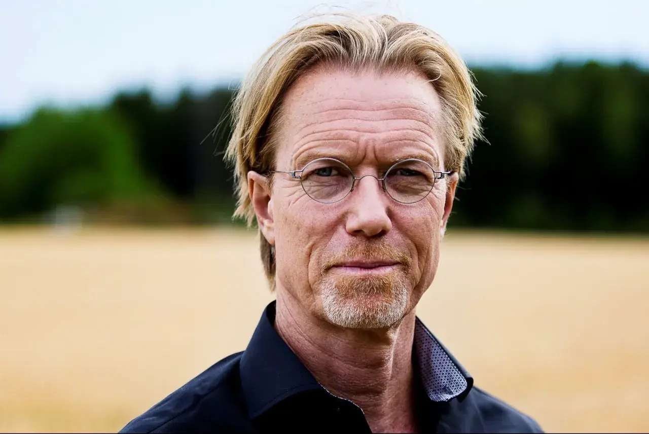 Ewert Grens, en man med blont hår och glasögon, ler mot kameran i en åker.