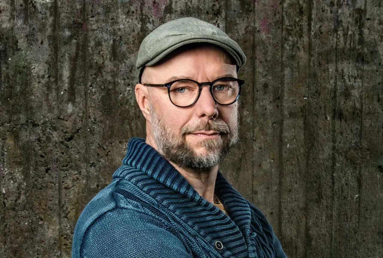 Sven Olov Karlsson, en man med glasögon och keps, blickar mot kameran. Han bär en blå stickad tröja.