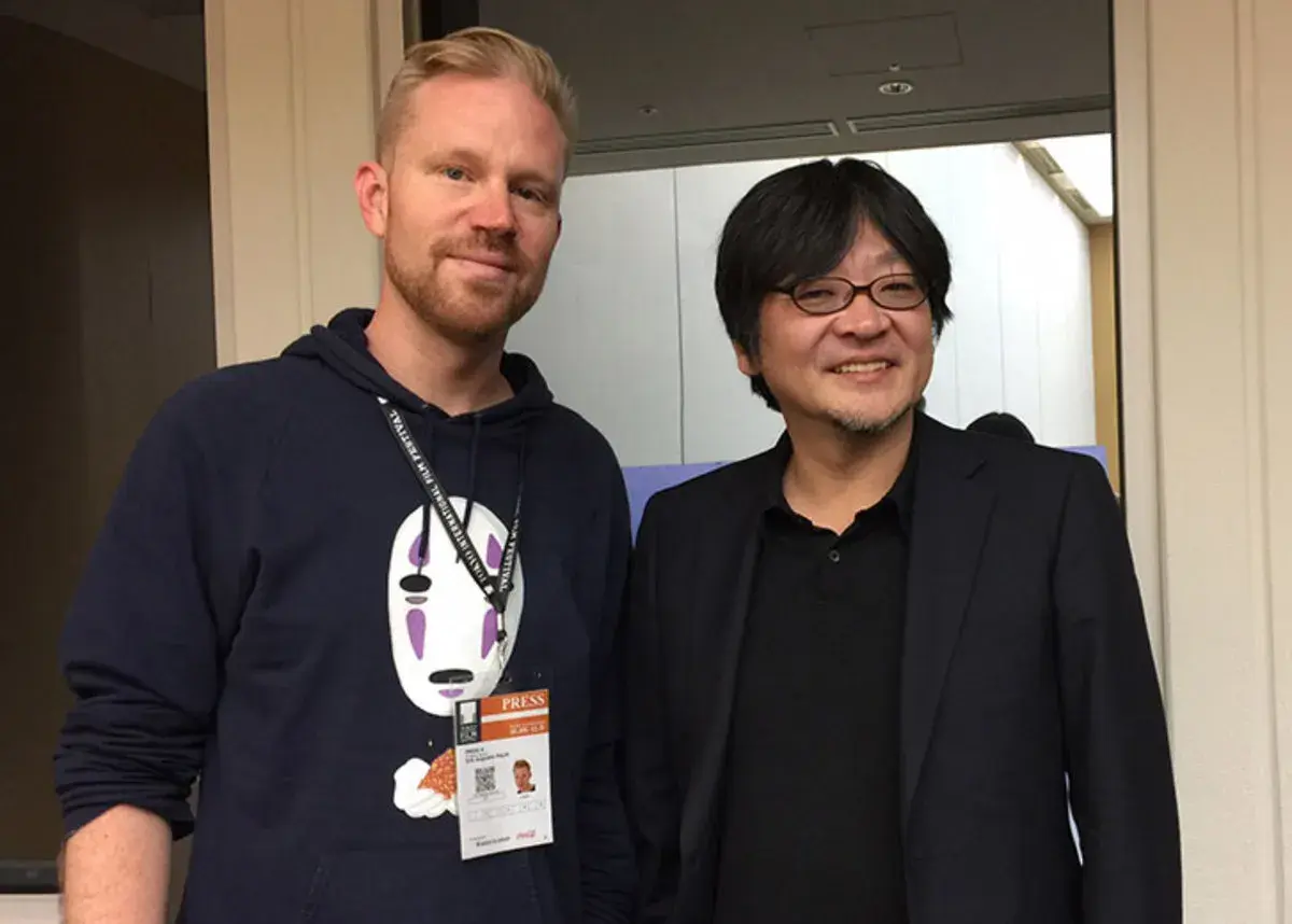 Erik Augustin Palm med en pressackreditering och en tröja med No-Face från Spirited Away, bredvid en japansk man i kostym.