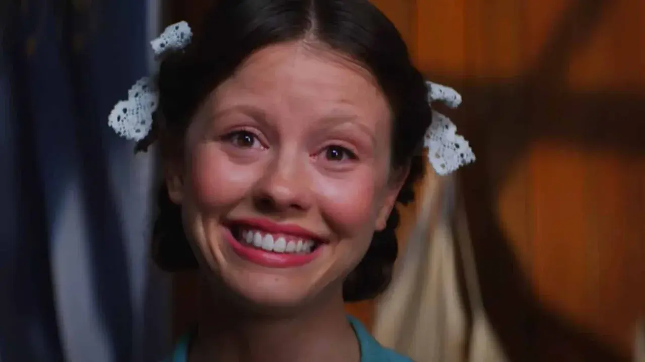 En närbild på Mia Goth som Pearl, med en bred, lite oroande leende och håret uppsatt med spets.