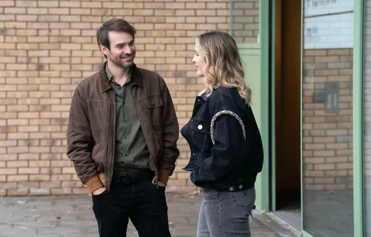Man och kvinna pratar utanför en byggnad, kanske en scen från en svensk kin serie.
