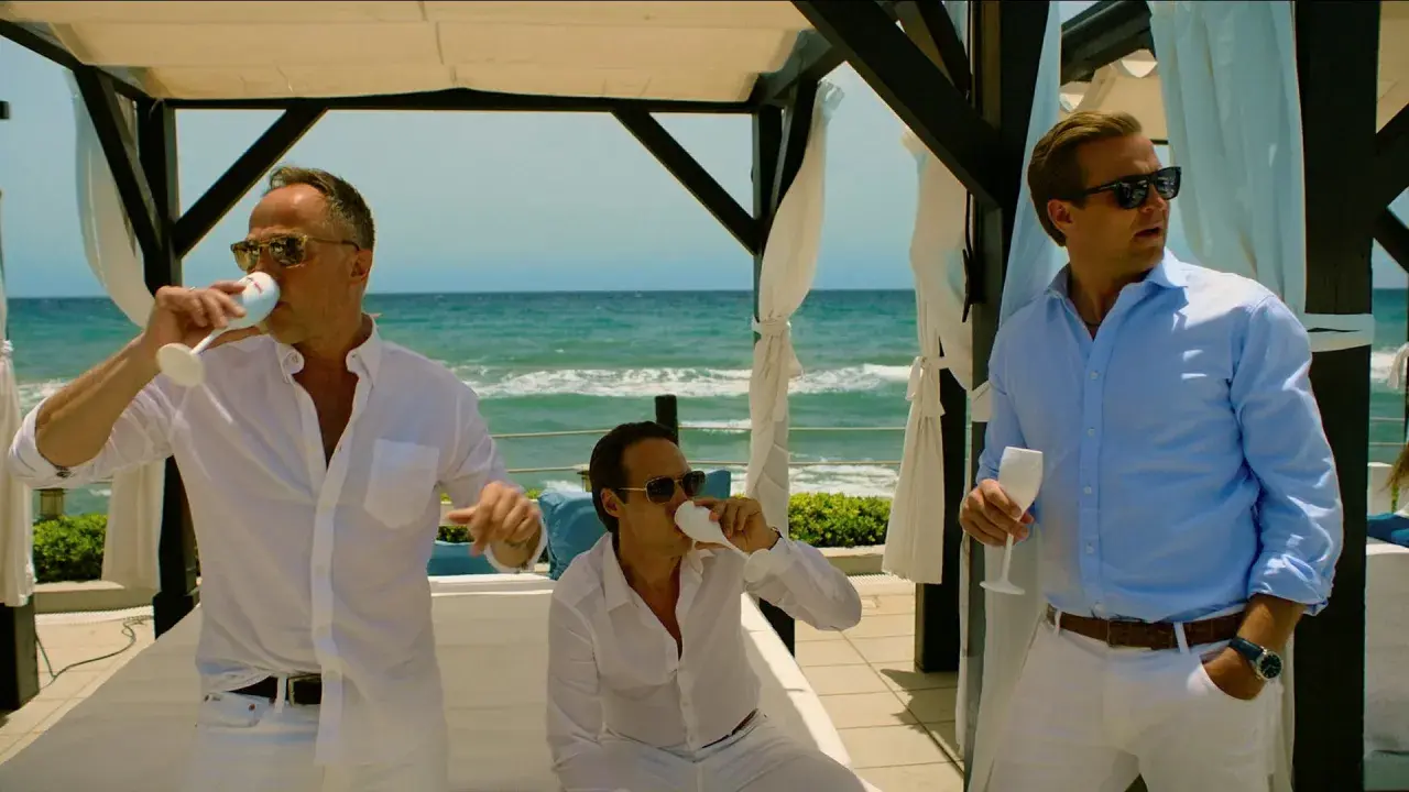 Tre män i vita och ljusblå skjortor dricker ur champagneglas vid havet. En scen från en exit serie.