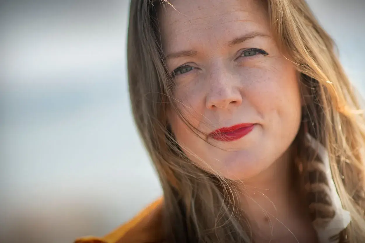 Tove Folkesson med rött läppstift och en fjäder i håret, fångad i ett mjukt ljus.