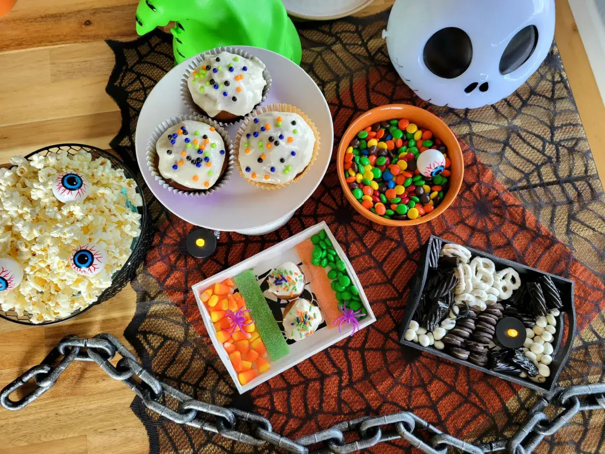 Söta godsaker för ett halloweenfilm barn. Cupcakes, popcorn med ögon och godis i en spöklik dukning.
