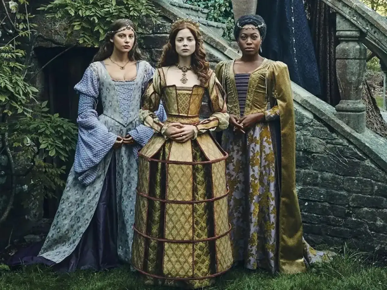 Tre kvinnor i magnifika historiska kläder, en kostymdrama serie som utspelar sig i en grönskande trädgård.