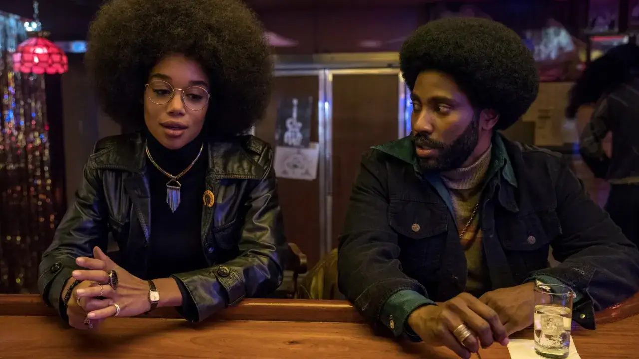 Ron och Patrice i Blackkklansman, med sina ikoniska frisyrer och kläder, sitter vid en bar och diskuterar.