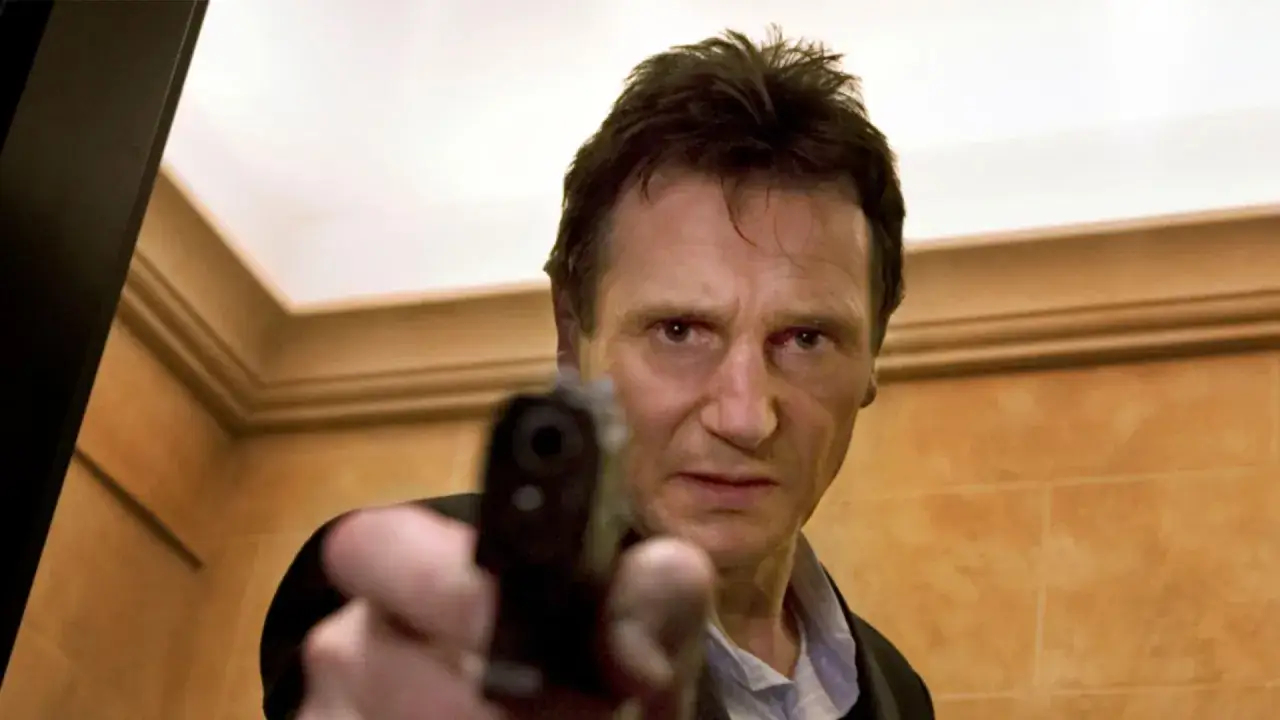 Liam Neeson siktar med en pistol, redo för action.