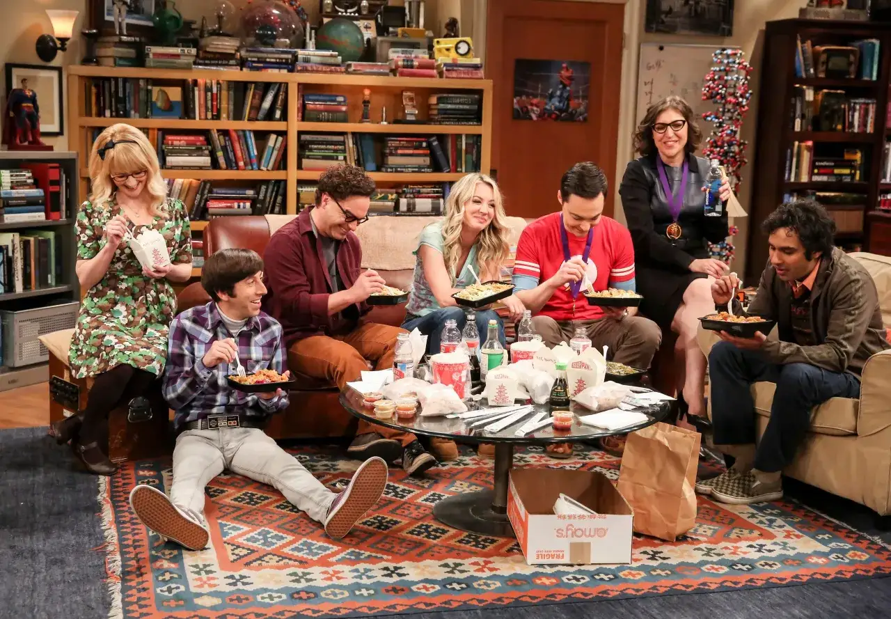 Rollistan i The Big Bang Theory samlas för en måltid. De sitter på golvet och soffan, omgivna av böcker och matlådor.