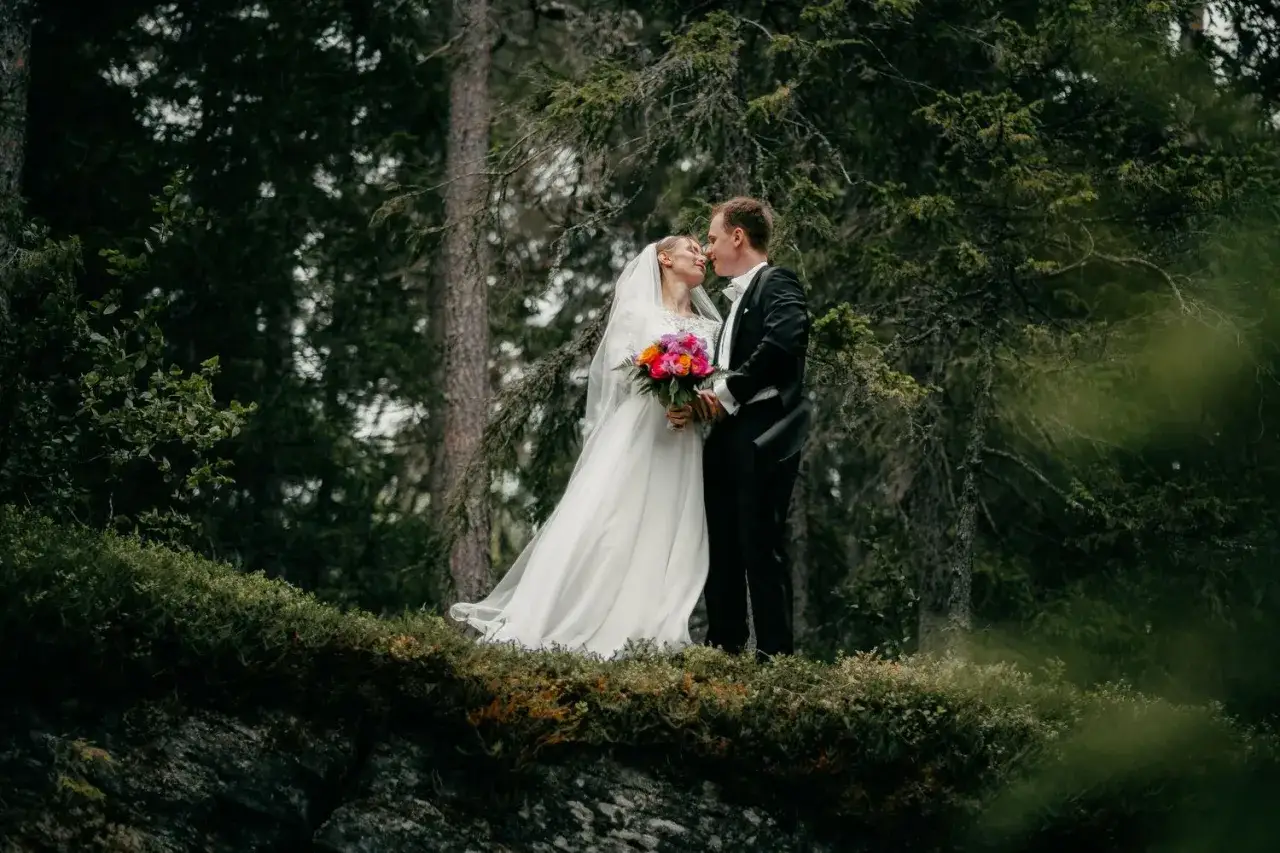 Br&ouml;llopspar, Frida Torgeby och hennes man, kysser varandra i en skog. Hon b&auml;r en vit kl&auml;nning och han en svart kostym.