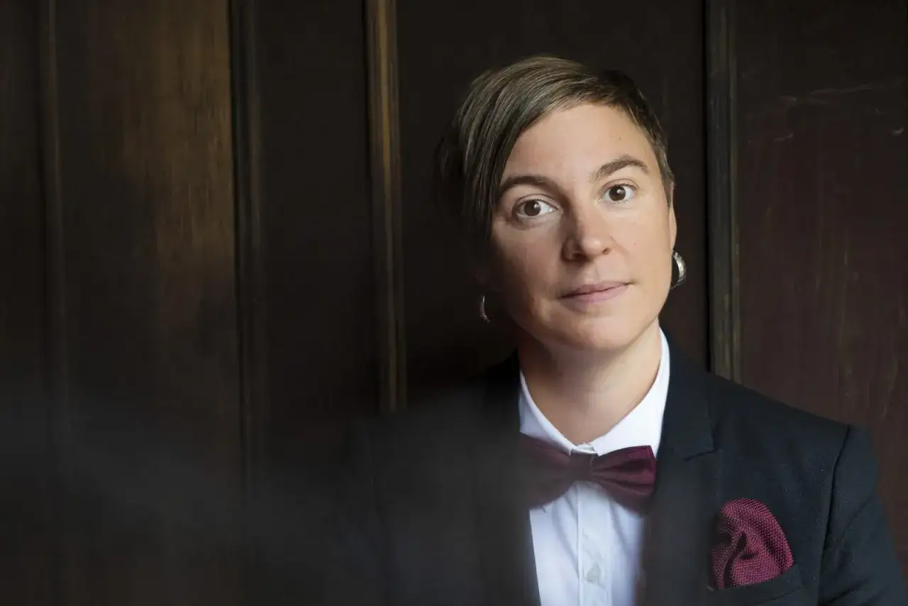 Elin Boardy, med kortklippt hår och en vinröd fluga, blickar mot kameran. Hon bär en svart kavaj och en vit skjorta.