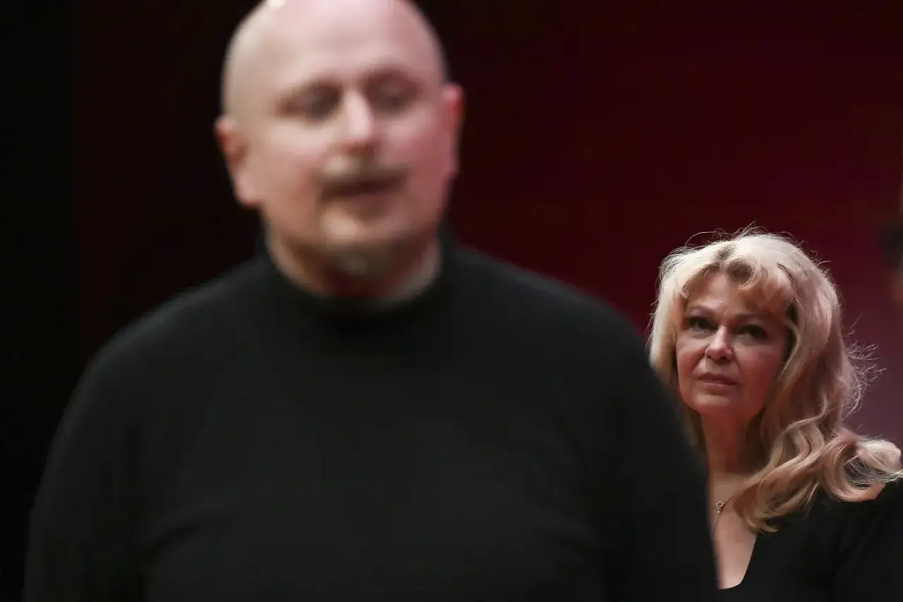 En kvinna med blont hår tittar mot kameran, möjligen Lars Noréns fru, medan en man i förgrunden är suddig.