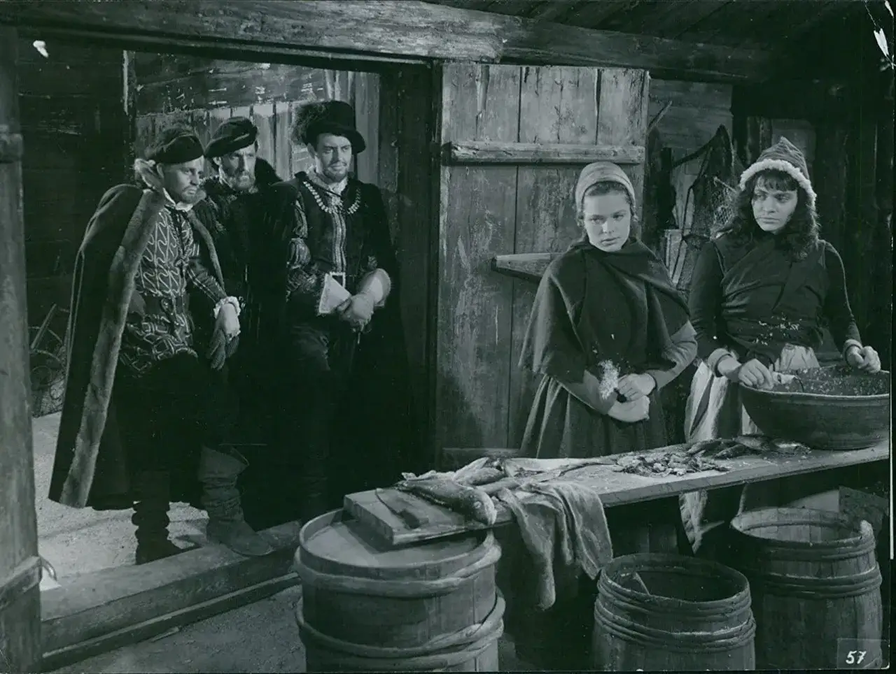 Scen från herr Arnes penningar film. Tre män i dräkter står i en dörröppning, medan två kvinnor arbetar med fisk.