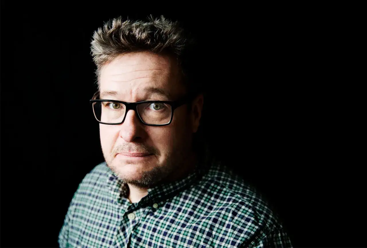 Kristian Lundberg, med glasögon och rutig skjorta, tittar in i kameran.