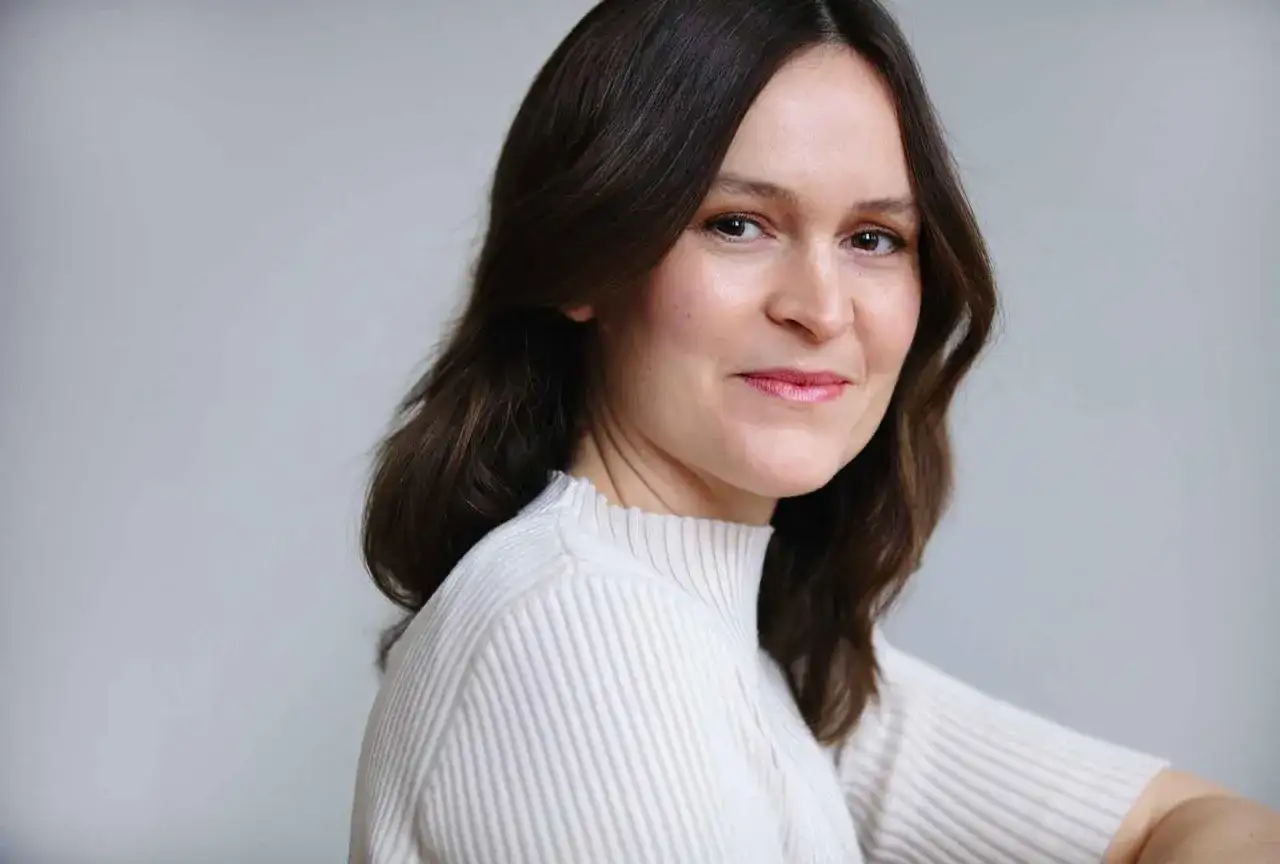 Elin Cullhed, en kvinna med mörkt hår och en vit stickad tröja, ler mjukt mot kameran.