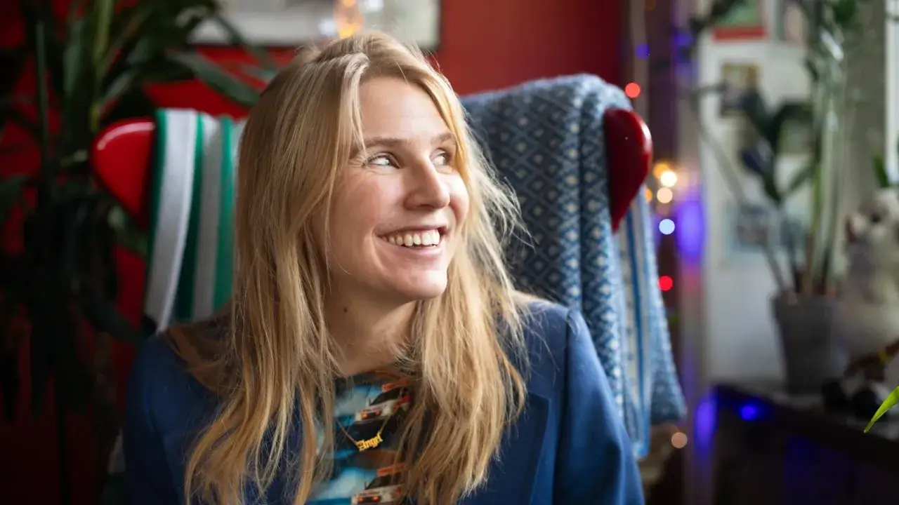 Amanda Romare ler glatt i en blå kavaj, omgiven av växter och julbelysning.