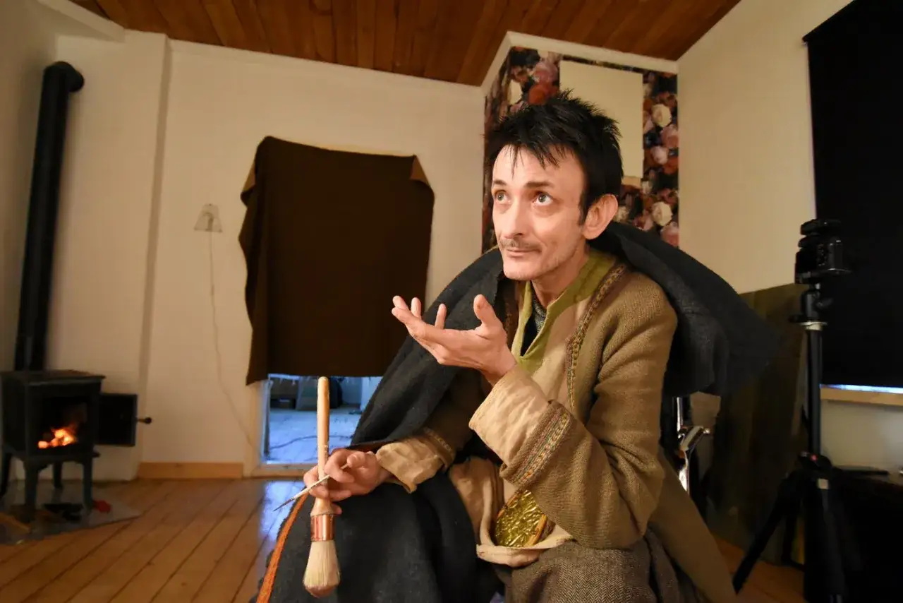 Andrea Lennartsson, med pensel och sax i hand, sitter vid en kamin och berättar.