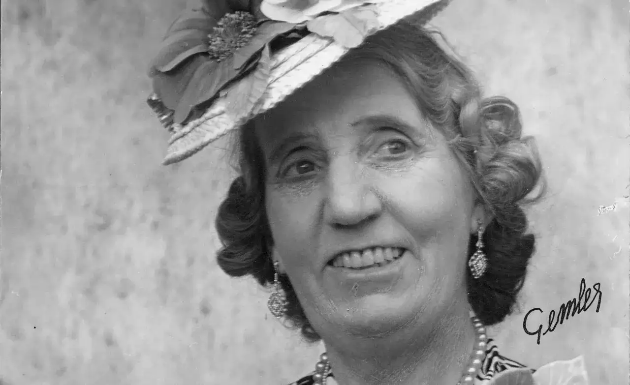 Julia Cæsar, en glad kvinna med hatt och örhängen, ler mot kameran.