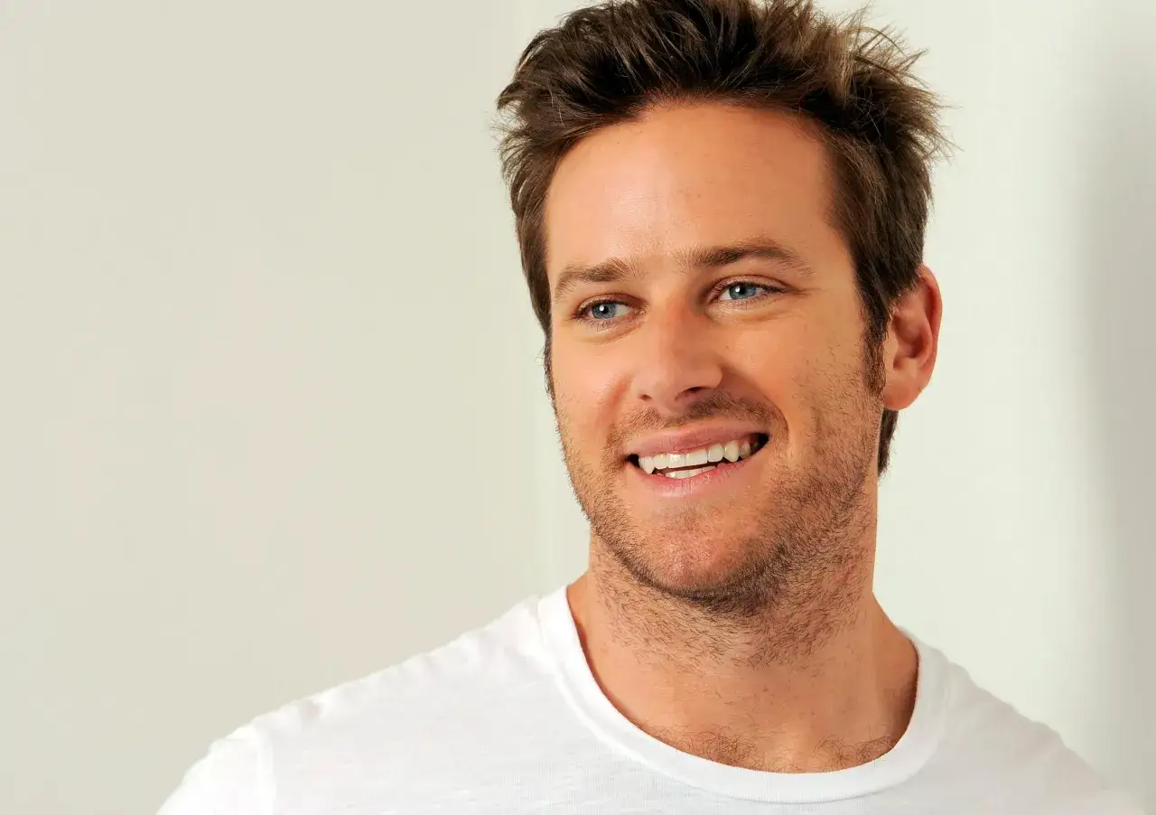 Armie Hammer ler med blå ögon och en vit t-shirt.