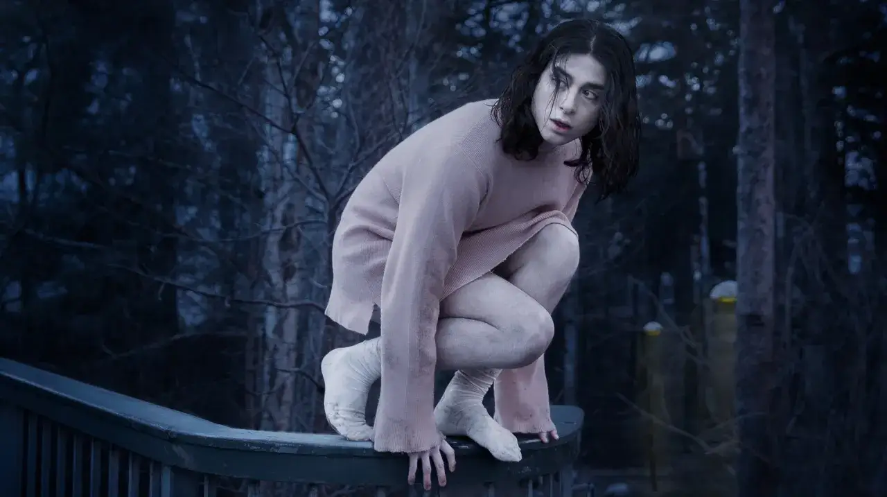 Svensk vampyr Eli hukar sig på ett räcke i en mörk skog, klädd i en rosa tröja och vita strumpor.