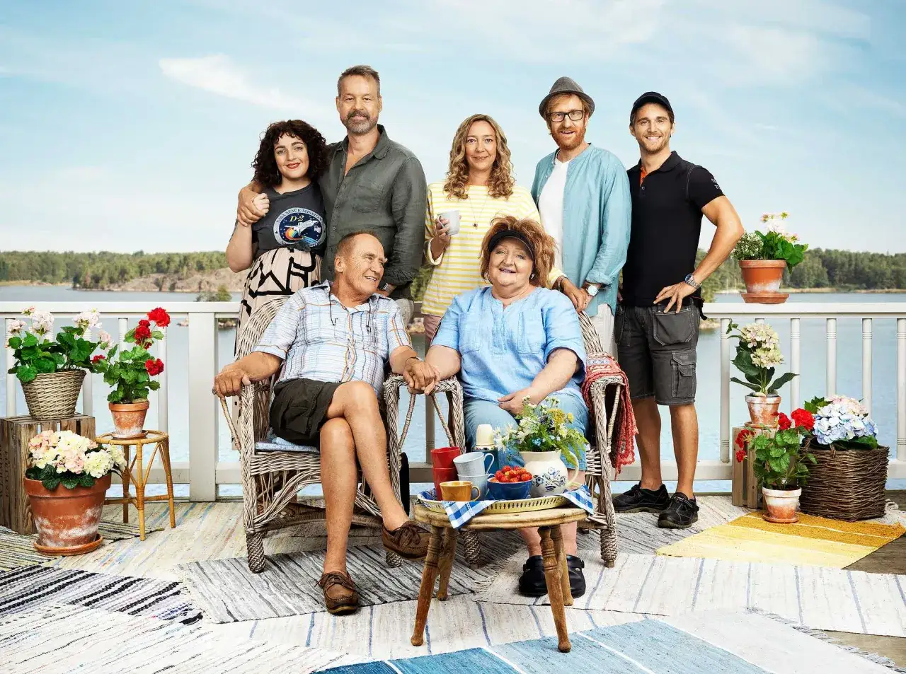 En familj samlad p&aring; en altan vid vattnet. De verkar njuta av varandras s&auml;llskap under udda veckor, kanske under semestern.